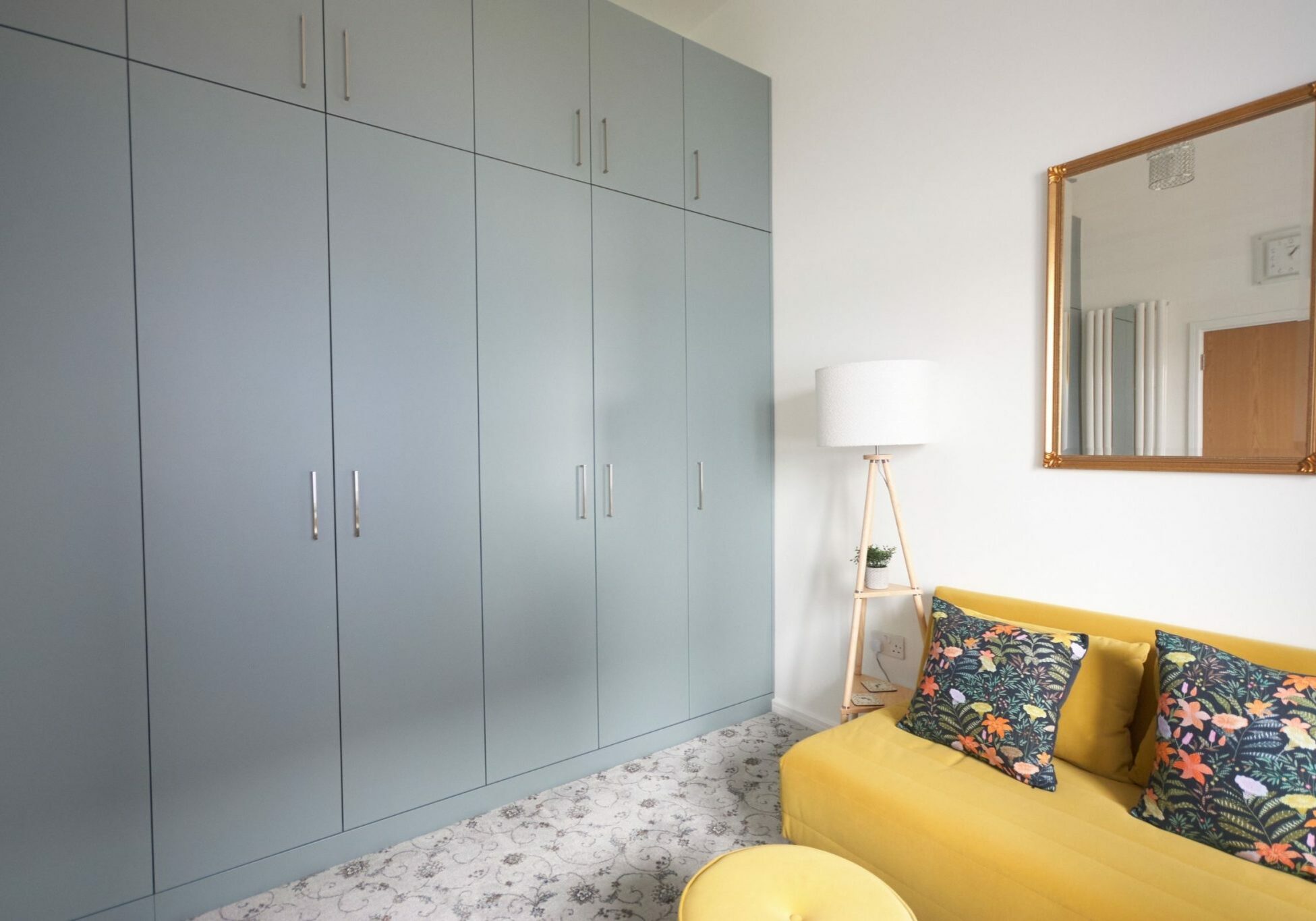 Blue-grey fitted wardrobes opening onto a mustard seating area